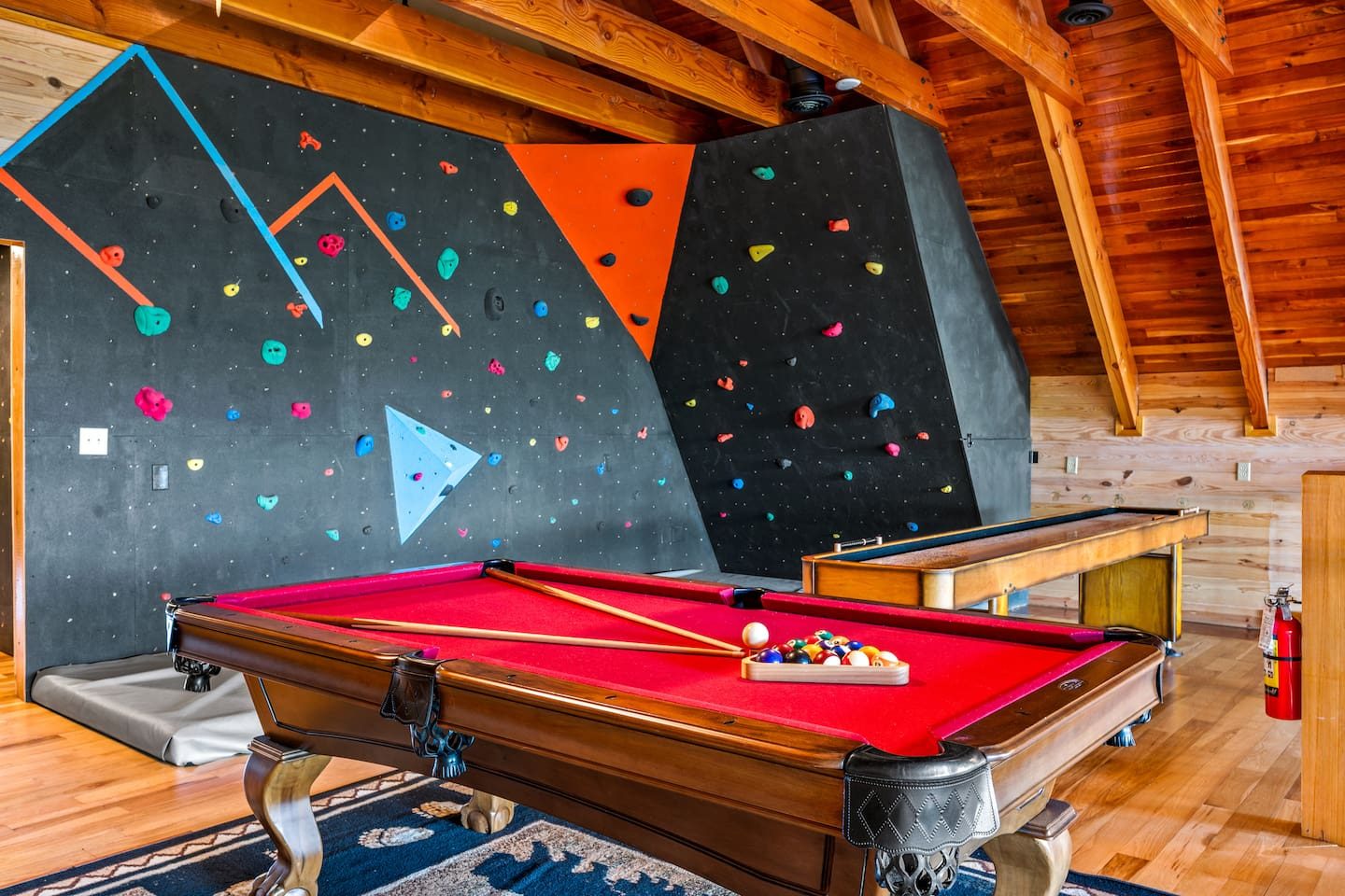 Rack 'em up! A red-felt billiards table sits beneath the climbing wall, with a shuffleboard table nearby. A game room made for playful rivalries.