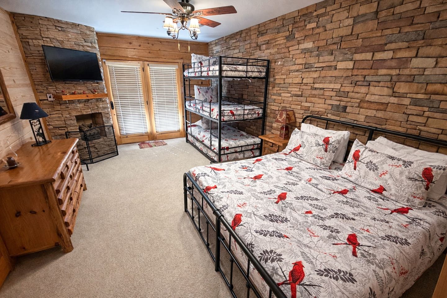 Cardinal-print bedding on a king bed, a snug bunk set nearby and a stone fireplace wall. Tuck in and let the Smokies lull you to sleep.