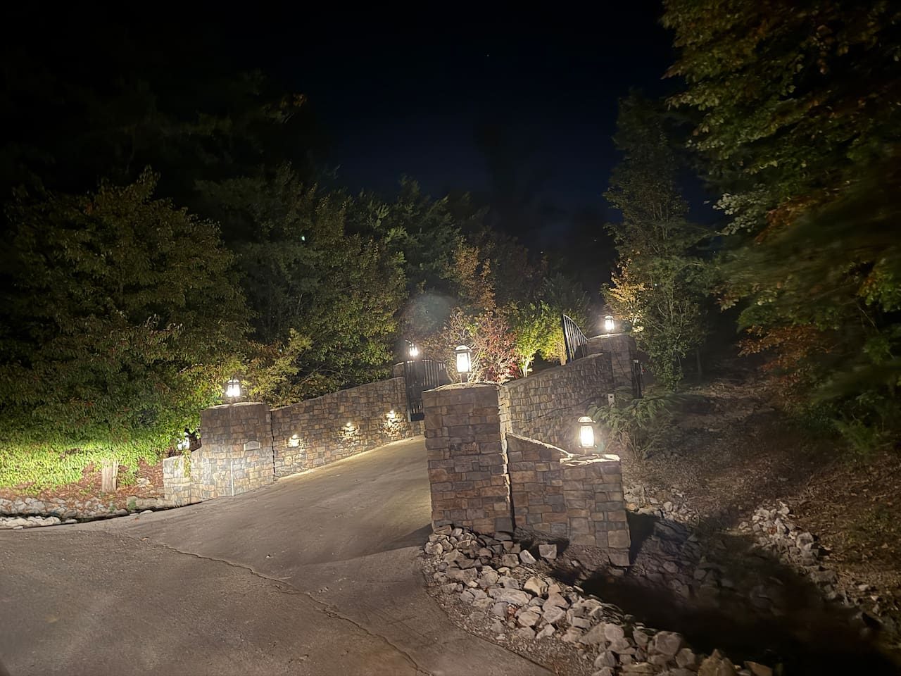 Softly lit stone walls guide the drive toward the lodge after dark. Arrive tired, and feel the mountain peace settle in at once.