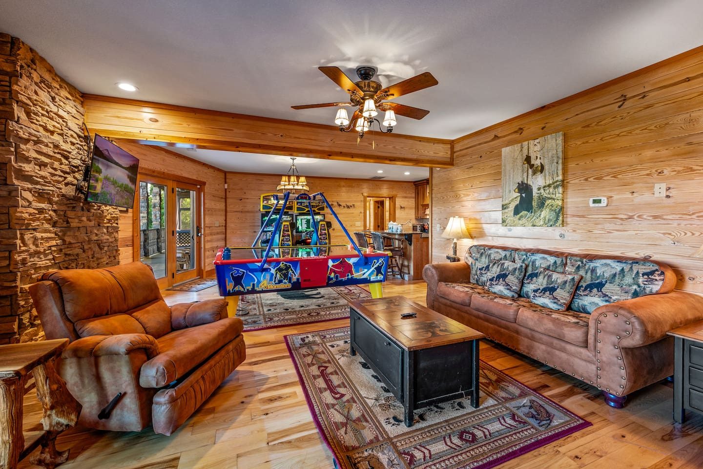 A snug game-room lounge with leather seats, a bright arcade glow in the distance and room to sprawl. Settle in with the whole crew.